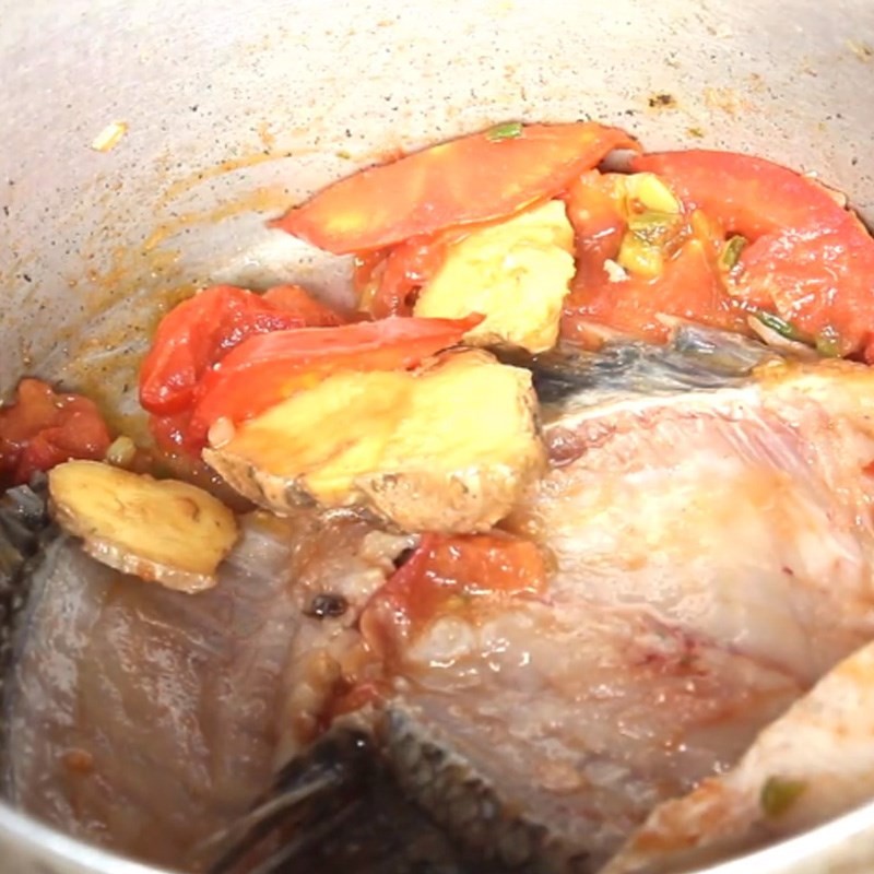 Xào cà chua và đầu hành lá trong nồi lẩu cá rô phi dưa chua để tạo màu và hương thơm.