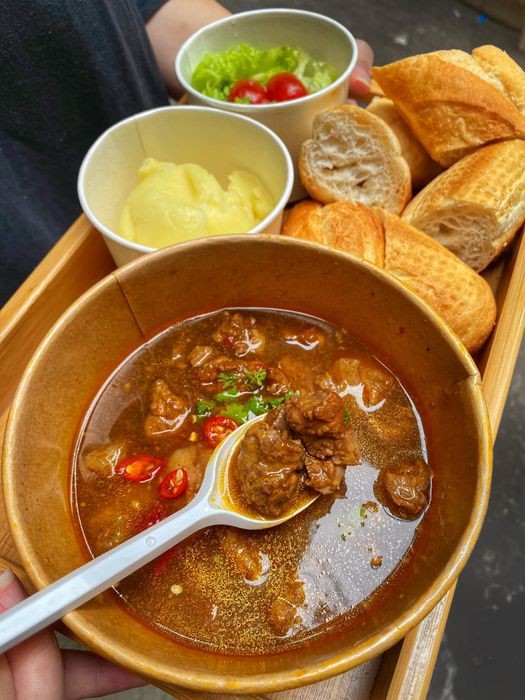 Bò sốt vang màu đỏ cam đặc trưng từ gấc, thịt bò hầm mềm rục ăn kèm rau thơm