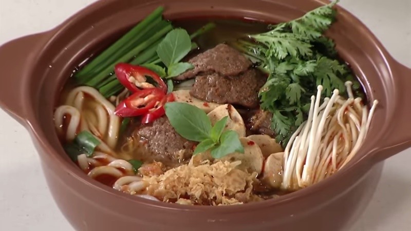 Tô mì cay chay thành phẩm, với sợi mì dai, nước dùng đỏ rực, bò lát chay, nấm kim châm và rau thơm tươi xanh