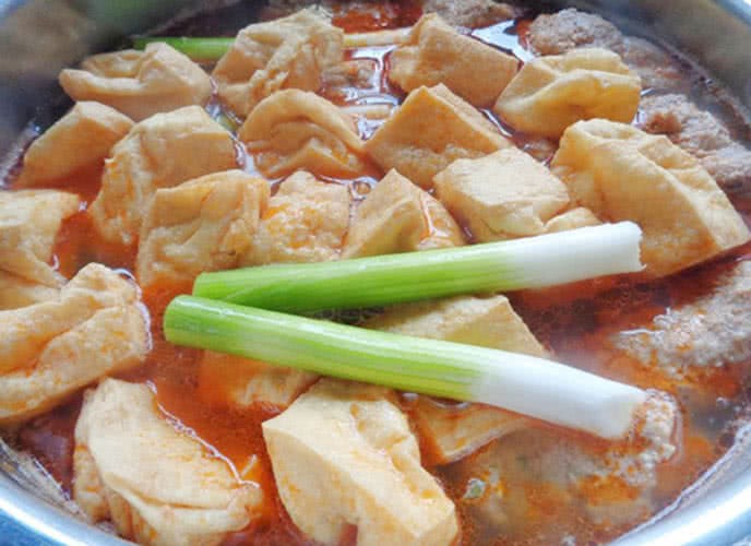 Nồi nước dùng canh bún đang được nấu, với riêu cua nổi lên và đậu phụ chiên hấp dẫn
