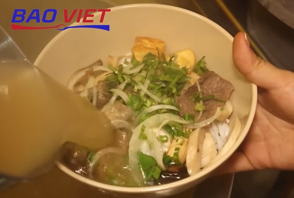 Chan nước dùng nóng hổi vào bát phở nấm chay đã xếp topping
