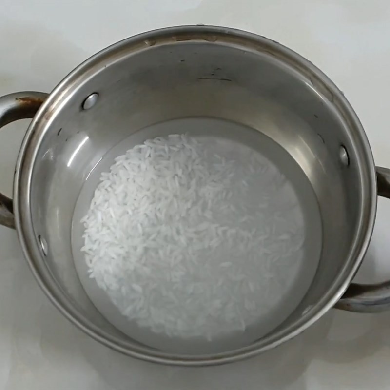 Gạo đã vo sạch, ngâm nước ấm trong nồi để chuẩn bị nấu cháo ngọt phô mai cho bé ăn dặm, giúp gạo nhanh nhừ