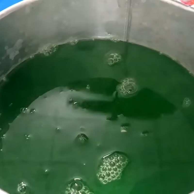 Một người đang dùng dao cắt khối rau câu lá dứa đã đông thành những miếng nhỏ trên thớt, chuẩn bị cho bước tiếp theo