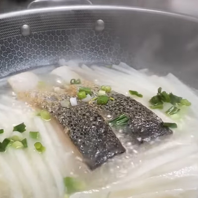 Thêm hành lá vào canh củ cải cá hồi trước khi tắt bếp