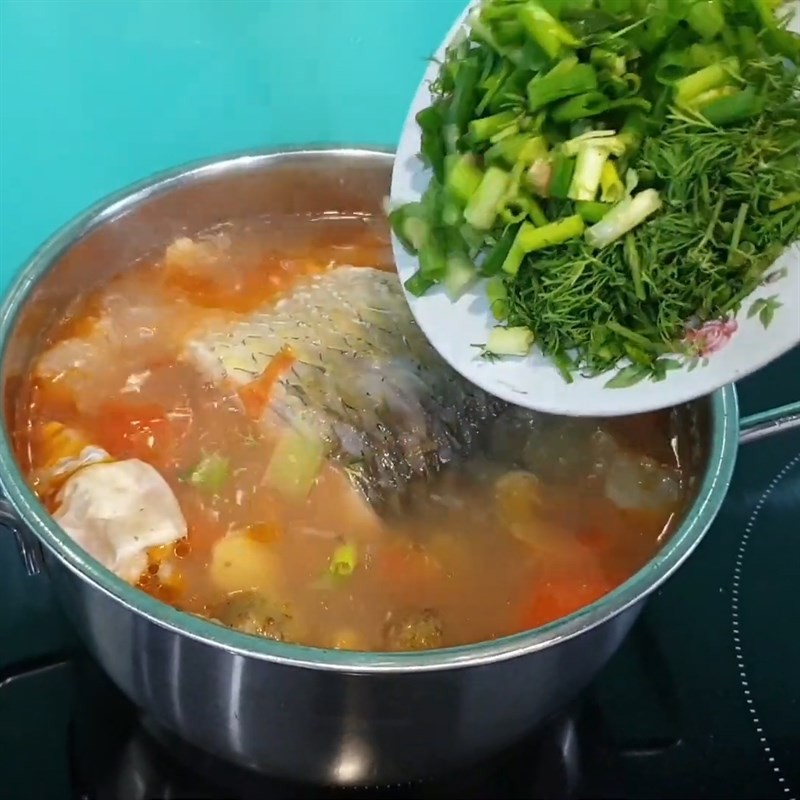 Thêm hành lá và thì là vào nồi canh cá trắm nấu sấu khi gần tắt bếp