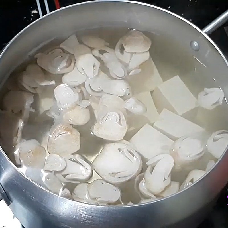 Thêm đậu hũ non vào nồi canh nấm, chờ nước sôi trở lại để tiếp tục nấu