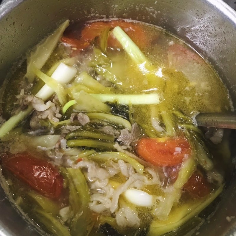 Thêm đầu hành lá vào canh dưa chua thịt bò trước khi tắt bếp