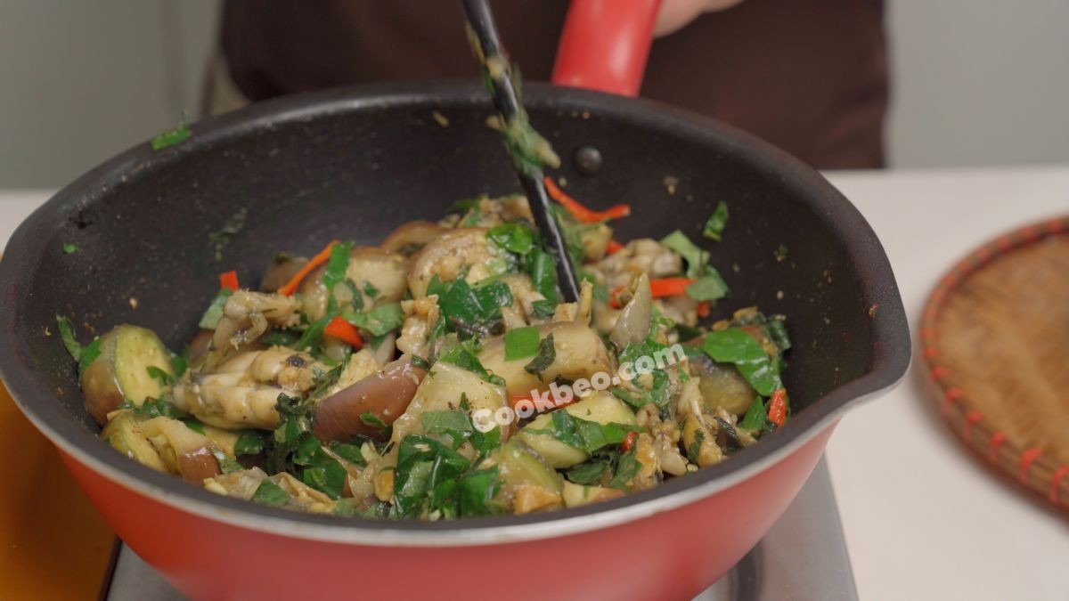 Món ếch xào cà tím gần hoàn thành, đang được thêm lá lốt, tía tô và ớt để tăng thêm hương vị và màu sắc