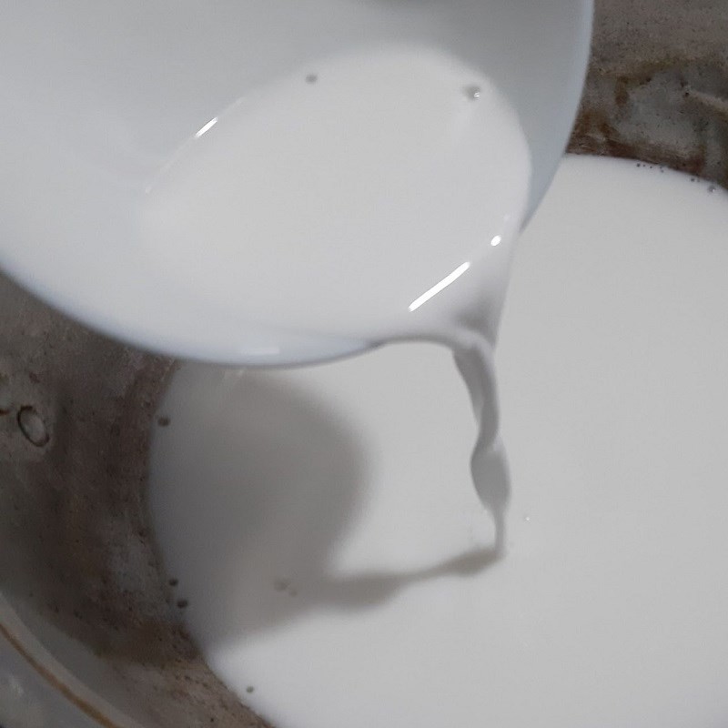 Nồi nước cốt dừa đang được đun trên bếp, thêm đường và muối để tạo vị đậm đà