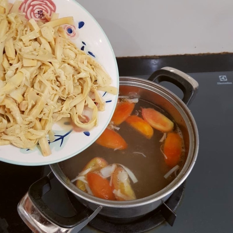 Thêm nước lọc vào cà chua đã xào để bắt đầu nấu phần nước dùng chính cho món bún ốc măng.
