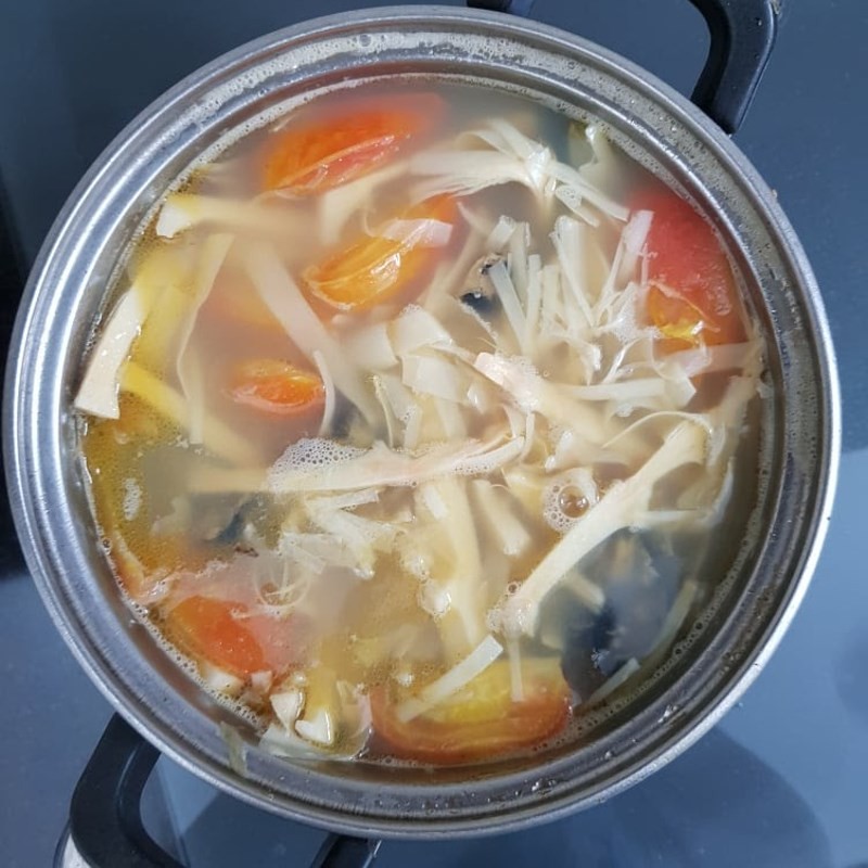 Cho thịt ốc và măng đã xào vào nồi nước dùng cà chua, hầm nhẹ để các nguyên liệu hòa quyện hương vị.