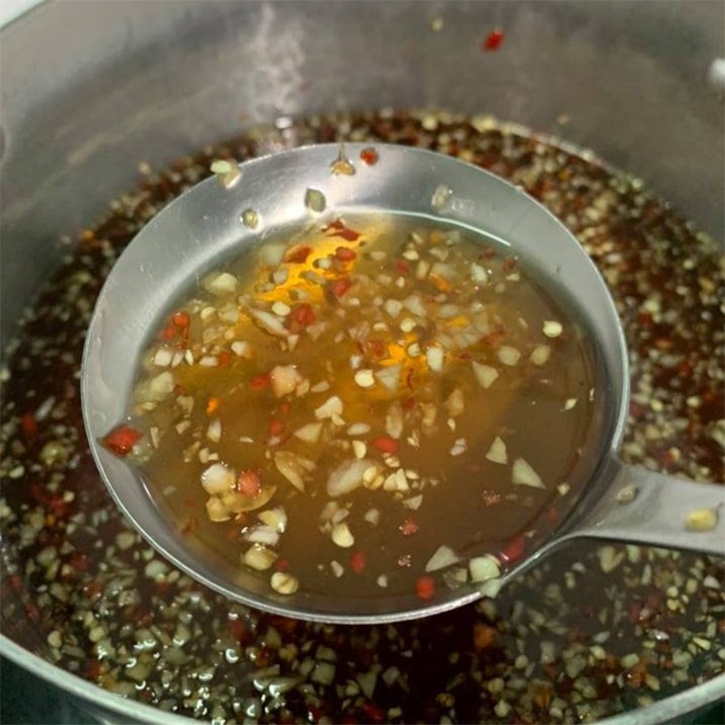 Hỗn hợp nước mắm đường được khuấy đều trên bếp để đảm bảo đường tan hoàn toàn.