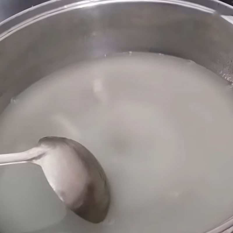Một người đang khuấy chất lỏng màu xanh lá cây trong nồi trên bếp, có thể là hỗn hợp rau câu và nước cốt lá dứa đang được đun sôi