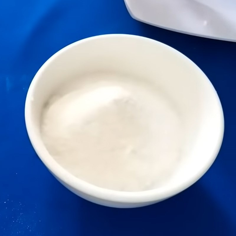 Một người đang dùng muỗng trộn đều bột rau câu và đường cát trong một chiếc chén sứ trắng