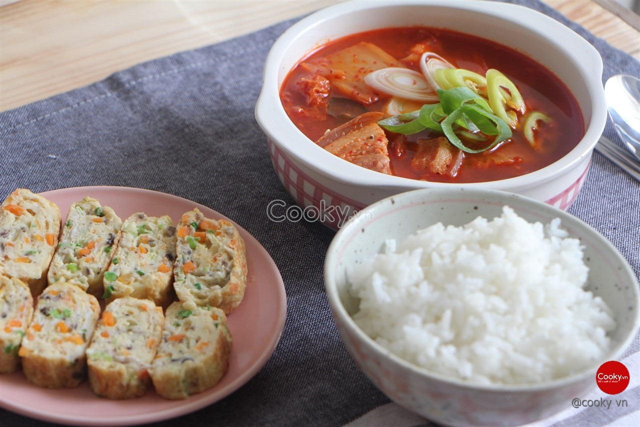 Món canh kim chi thịt ba chỉ đã hoàn thành, được trang trí với hành boa rô và ớt tươi, sẵn sàng để thưởng thức