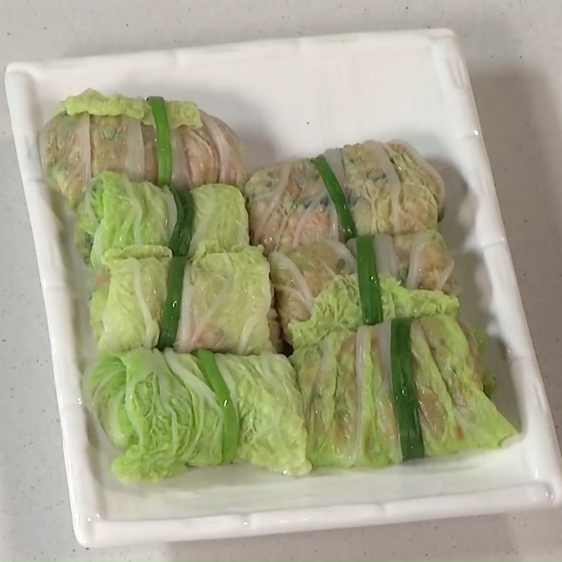 Cố định các cuộn cải thảo nhân thịt bằng hành lá đã trụng, giữ cho nhân không bung ra khi nấu.