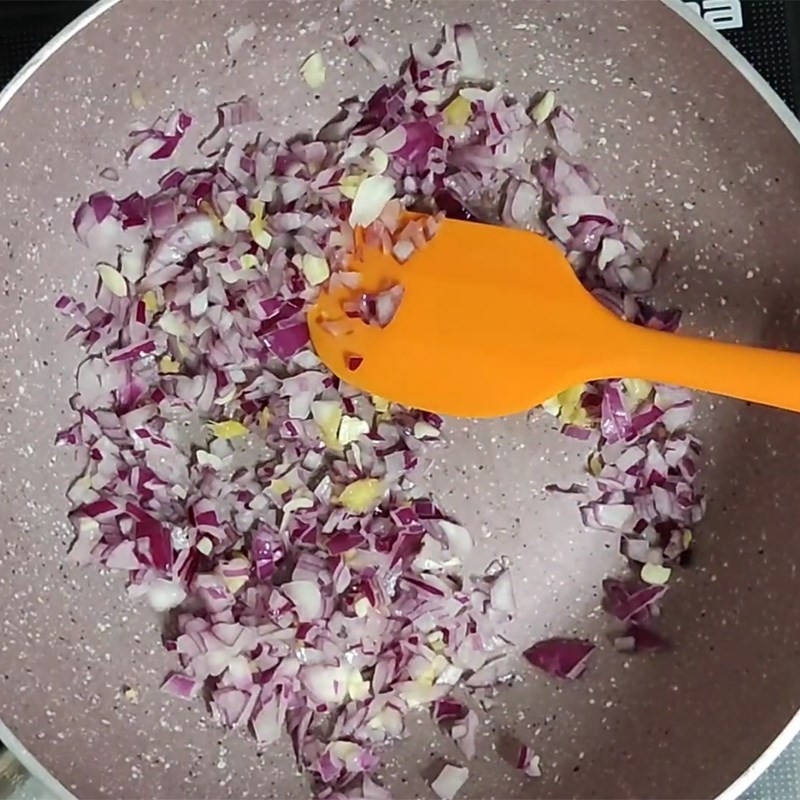 Phi thơm hành tím và lá nguyệt quế trong chảo, tạo mùi vị đặc trưng cho canh bắp cải cà chua xay