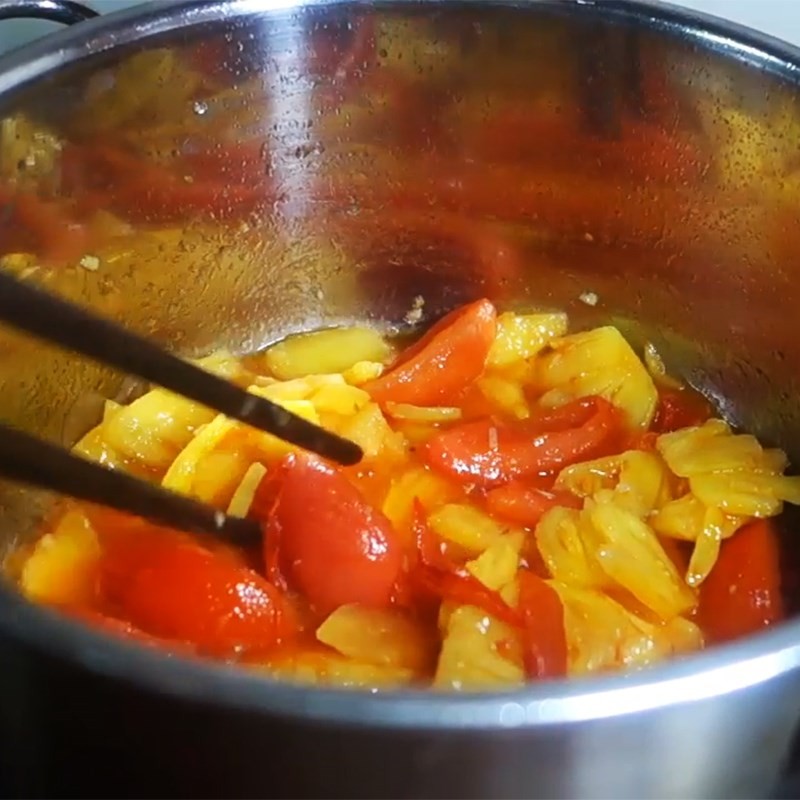 Cà chua và thơm đang được xào thơm trên bếp, tạo màu sắc và hương vị chua ngọt đặc trưng cho nước dùng bún cá cam