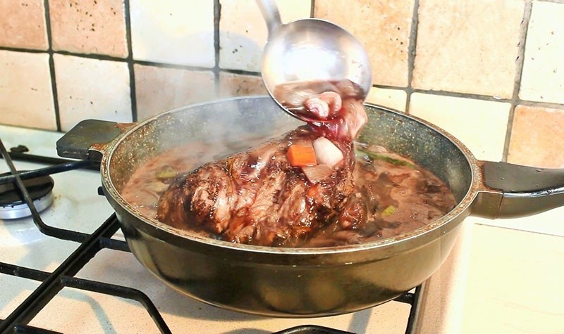 Món bò hầm rượu vang đang được nấu trên bếp, với nước sốt sánh mịn và hương thơm hấp dẫn
