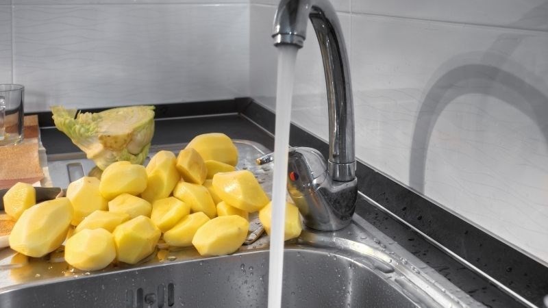 Rửa khoai tây đã bào sạch dưới vòi nước để loại bỏ nhựa, chuẩn bị nấu canh