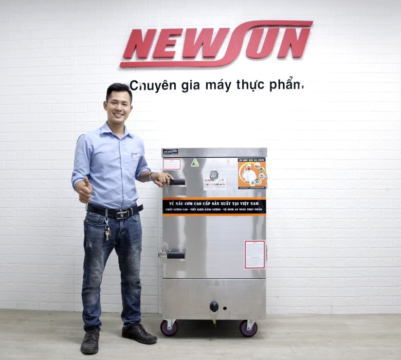 Mô tả: Một chuyên gia đang hướng dẫn cách nấu cơm bằng tủ công nghiệp với các khay cơm xếp chồng lên nhau.