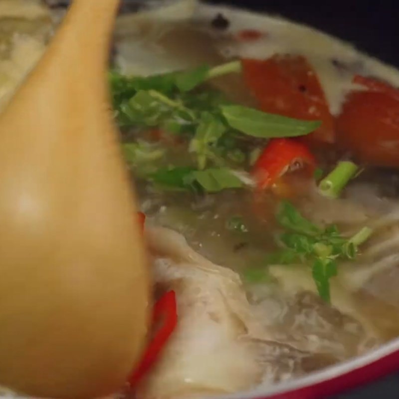 Rắc rau thơm và ớt sừng vào món canh cá lăng nấu măng chua