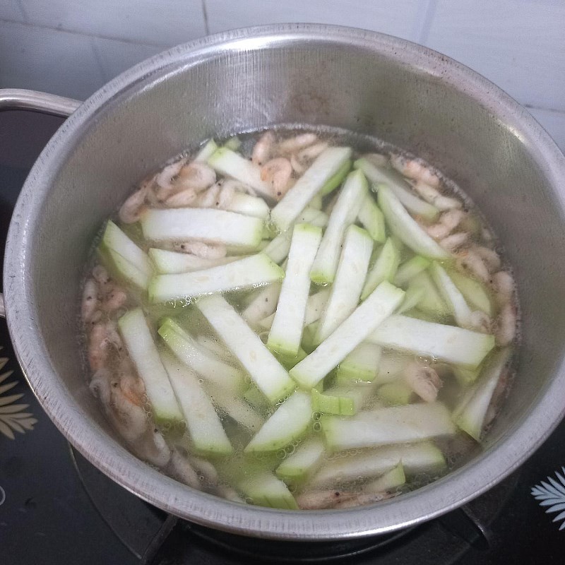 Cho bầu đã cắt vào nồi canh tép đang sôi để bầu chín tới