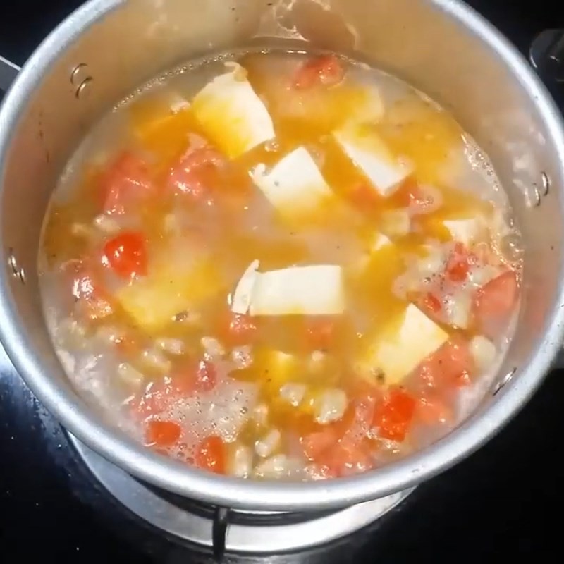 Đậu phụ được thêm vào nồi canh ngao cà chua đang sôi, sẵn sàng thấm vị