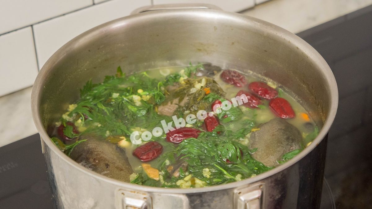 Nồi gà với ngải cứu đang được hầm trên bếp với lửa nhỏ, đảm bảo nước dùng trong và gà mềm