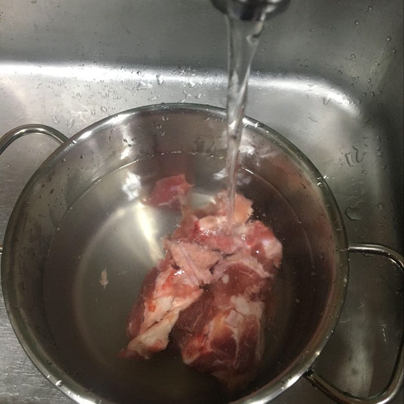 Hình ảnh sơ chế xương heo, rửa sạch dưới vòi nước chuẩn bị nấu mì xương ngon