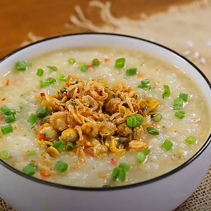 Tô cháo hến xào cay đã hoàn thành, trang trí với rau thơm, hành phi và ớt.