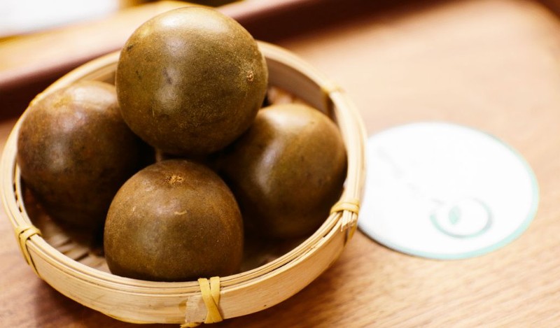 Một người phụ nữ tươi cười đang cầm một quả La Hán khô, biểu thị việc sử dụng loại quả này để hỗ trợ giảm cân và sức khỏe.