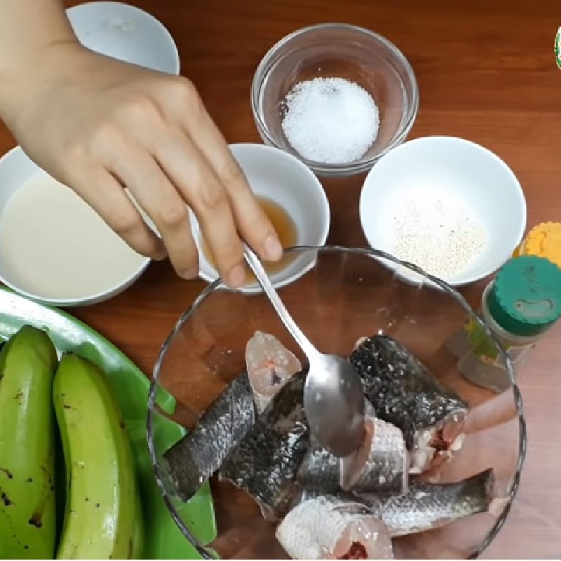 Ướp cá lóc với hành tím băm, bột nghệ, muối, hạt nêm và tiêu để cá thấm vị trước khi nấu chuối xanh