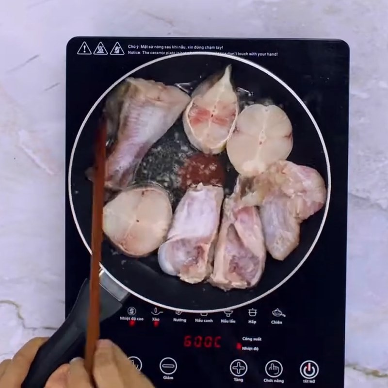 Cá lăng đang được xào trên chảo, chuẩn bị cho nồi canh