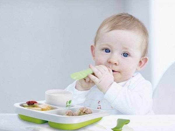Bé 10 tháng tuổi đang tự ăn dặm, thể hiện sự hứng thú với việc khám phá món ăn trong giai đoạn phát triển