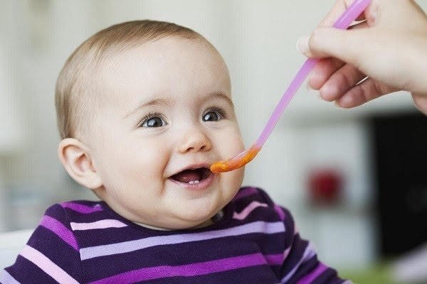 Bé 4 tháng tuổi đang quan sát một chiếc thìa nhỏ màu xanh lá cây, ám chỉ dấu hiệu sẵn sàng ăn dặm.