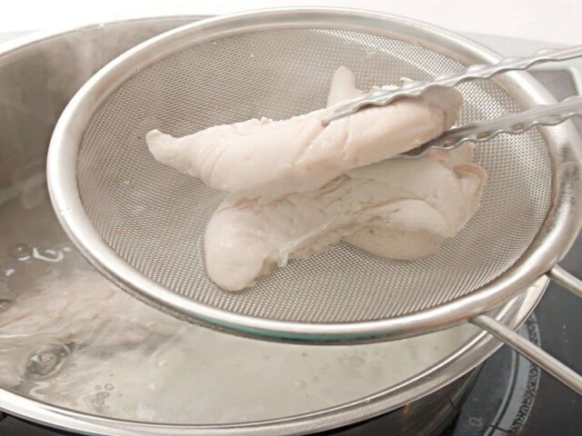 Thịt gà đang luộc trong nồi để nấu cháo thịt gà bí đỏ cho bé