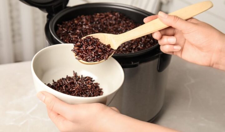 Gạo lứt huyết rồng đã nấu trong nồi cơm điện, với thìa gỗ
