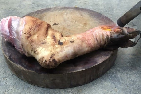 Chân giò heo đang được thui vàng trên bếp, chuẩn bị nấu món giả cầy miền Trung